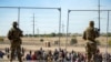 Migrantes esperan junto a una valla fronteriza bajo la vigilancia de la Guardia Nacional de Texas, el 10 de mayo de 2023, para ingresar a El Paso. (AP/Andrés Leighton)