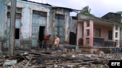 Dos hombres limpian escombros en una casa que ha sido parcialmente destruida por el paso del huracán "Sandy", en la ciudad de Guantánamo (Cuba).