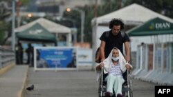 Steve Oliveros conduce a su madre en silla de ruedas de vuelta a Colombia tras serle negado el paso en la frontera para entrar a Venezuela.