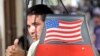 Un hombre saluda desde una bicitaxi con la bandera de EEUU.
