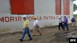 Delegación extranjera pasea frente a un mural con estrofas del himno nacional cubano.