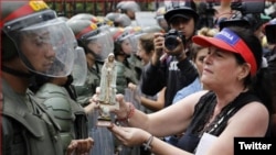 Una madre venezolana ofrece una estatuilla de la virgen a un efectivo de la Guardia Nacional Bolivariana.